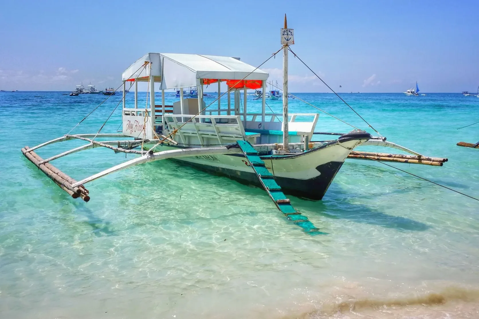 Un bateau traditionnel ancré dans une eau turquoise au large d'une plage blanche.