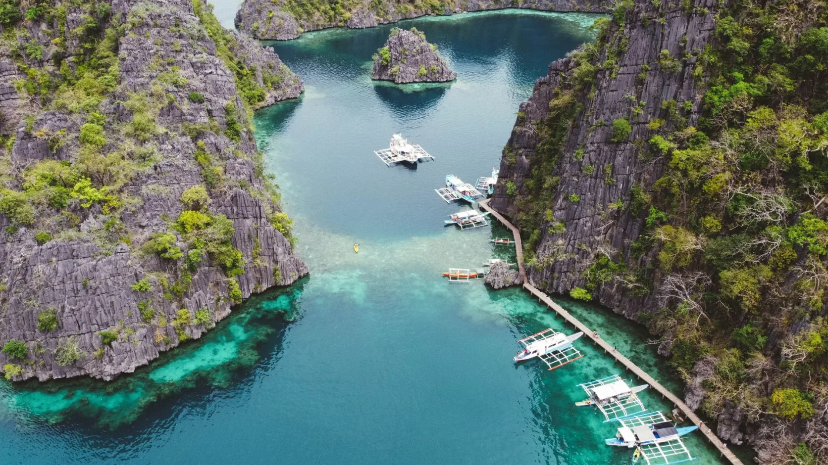 Des bateaux dans une eau transparente entre les falaises de Coron, vus du ciel.