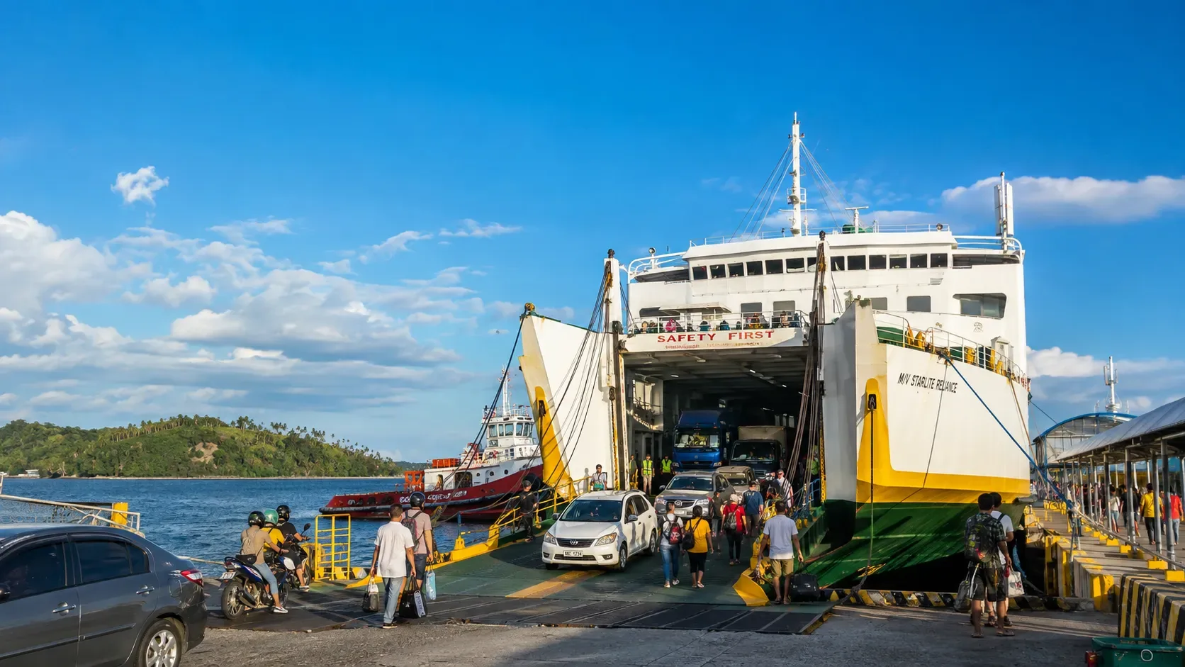 Un ferry roll-on roll-off embarquant des véhicules dans un port philippin, rampe abaissée et voitures faisant la queue pour monter à bord.