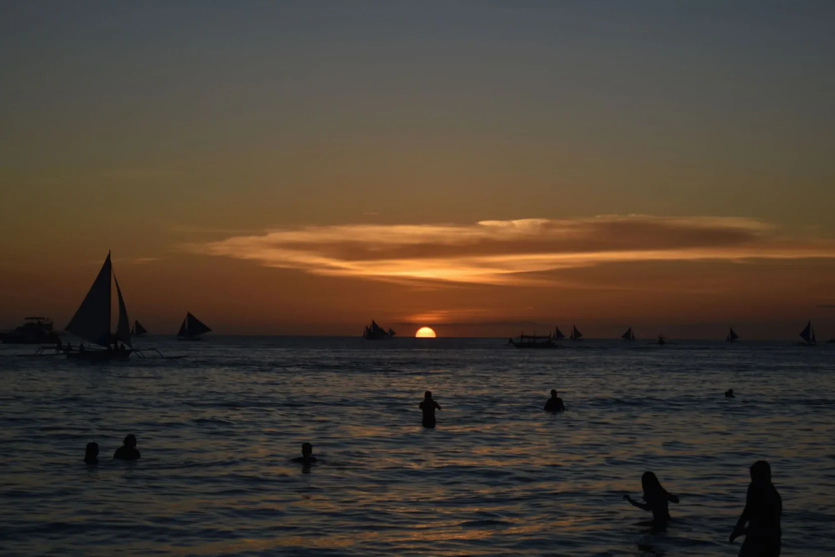 Des bateaux et des baigneurs au coucher du soleil au large d'une plage tropicale.